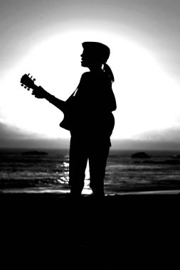 Tanımlanamayan genç bir kadın Laguna Beach California 'da güneş batarken gitarını çalıyor. Akustik gitarlı bir kız. Herkes için müzik çalmak. Gün batımında müzik çalan ve şarkı söyleyen bir kızla. Kaliforniya Günbatımı. 