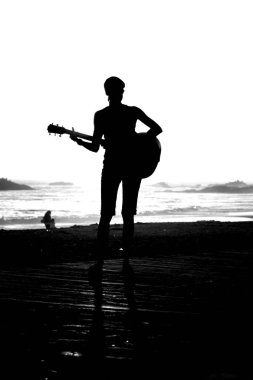 Tanımlanamayan genç bir kadın Laguna Beach California 'da güneş batarken gitarını çalıyor. Akustik gitarlı bir kız. Herkes için müzik çalmak. Gün batımında müzik çalan ve şarkı söyleyen bir kızla. Kaliforniya Günbatımı. 