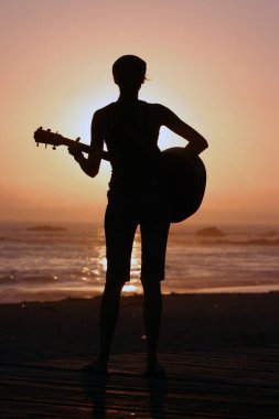 Tanımlanamayan genç bir kadın Laguna Beach California 'da güneş batarken gitarını çalıyor. Akustik gitarlı bir kız. Herkes için müzik çalmak. Gün batımında müzik çalan ve şarkı söyleyen bir kızla. Kaliforniya Günbatımı. 