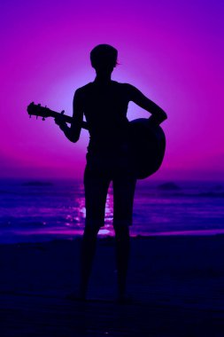 Tanımlanamayan genç bir kadın Laguna Beach California 'da güneş batarken gitarını çalıyor. Akustik gitarlı bir kız. Herkes için müzik çalmak. Gün batımında müzik çalan ve şarkı söyleyen bir kızla. Kaliforniya Günbatımı. 
