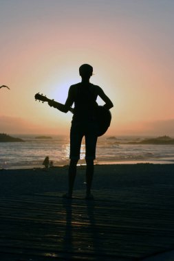Tanımlanamayan genç bir kadın Laguna Beach California 'da güneş batarken gitarını çalıyor. Akustik gitarlı bir kız. Herkes için müzik çalmak. Gün batımında müzik çalan ve şarkı söyleyen bir kızla. Kaliforniya Günbatımı. 