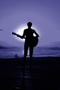 Tanımlanamayan genç bir kadın Laguna Beach California 'da güneş batarken gitarını çalıyor. Akustik gitarlı bir kız. Herkes için müzik çalmak. Gün batımında müzik çalan ve şarkı söyleyen bir kızla. Kaliforniya Günbatımı. 