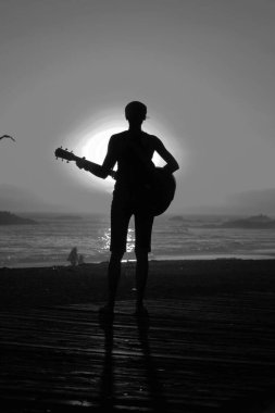 Tanımlanamayan genç bir kadın Laguna Beach California 'da güneş batarken gitarını çalıyor. Akustik gitarlı bir kız. Herkes için müzik çalmak. Gün batımında müzik çalan ve şarkı söyleyen bir kızla. Kaliforniya Günbatımı. 