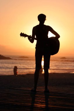 Tanımlanamayan genç bir kadın Laguna Beach California 'da güneş batarken gitarını çalıyor. Akustik gitarlı bir kız. Herkes için müzik çalmak. Gün batımında müzik çalan ve şarkı söyleyen bir kızla. Kaliforniya Günbatımı. 