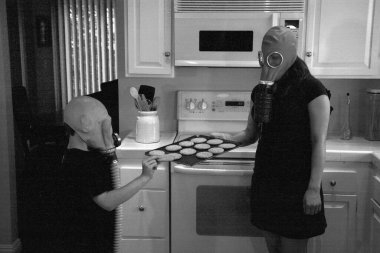 a mother and son enjoy peanut butter cookies in their kitchen while wearing gas masks in a post nuclear winter future. Global Warming Cookie Day. A young family enjoys Cookies while wearing Gas Masks due to Global Warming. After school snack. cookies