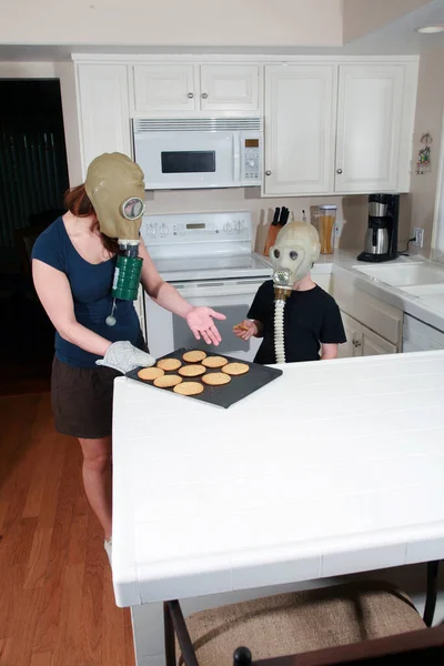 a mother and son enjoy peanut butter cookies in their kitchen while wearing gas masks in a post nuclear winter future. Global Warming Cookie Day. A young family enjoys Cookies while wearing Gas Masks due to Global Warming. After school snack. cookies