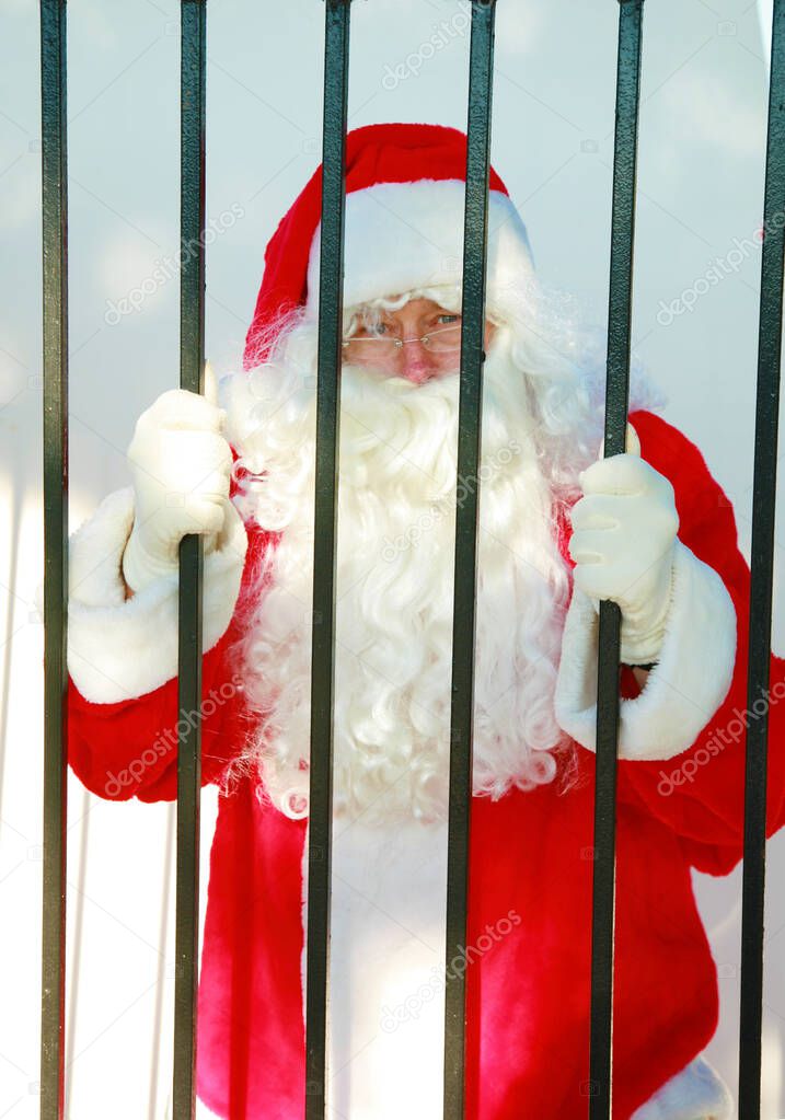 Santa Claus standing in a jail cell behind bars. isolated on white. Santa Claus Christmas. Santa Claus Mug Shot. Santa is arrested. Santa Claus Christmas. Santa Claus Mug Shot. Santa is arrested and his Mug Shot photo taken. Sad Santa Claus.