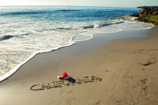 California 这个词写在沙滩上的沙滩上 带着圣诞老人的帽子和海浪 一个充满欢乐和 加利福尼亚 字样的加州圣诞 加州的圣诞节圣诞快乐 祝大家节日快乐 — 图库照片