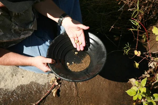 gold panning. A man striking it rich by finding the mother lode or at least a nugget or two. golden nuggets gold pan in the water. Old gold panning equipment. finding lost gold. Alaska gold. Gold Rush. Gold in the ground. Gold Mine. Golden Future.