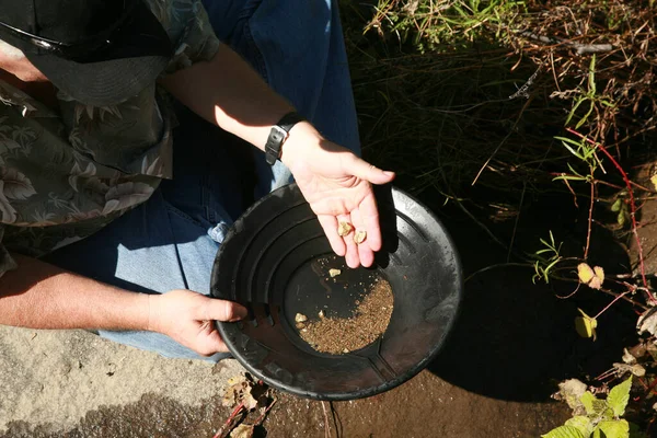 gold panning. A man striking it rich by finding the mother lode or at least a nugget or two. golden nuggets gold pan in the water. Old gold panning equipment. finding lost gold. Alaska gold. Gold Rush. Gold in the ground. Gold Mine. Golden Future.