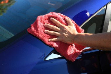 Araba yıkama, ıslak araba kurutma. Yıkanmış bir arabayı kurutmak. Araba detayı. Garaj yolunda araba yıkama. Temiz havlu. Arabayı yıkadıktan sonra adam. Araba yıkamada mavi arabayı kırmızı bir bezle siliyor. Erkek eli ve araba gövdesi yakın.. 
