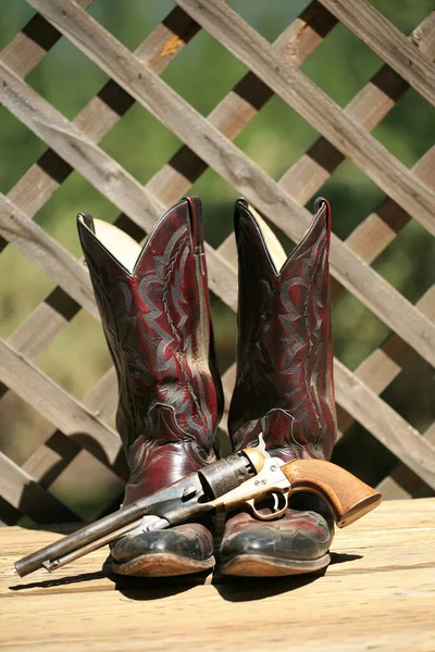 Cowboy Boots. Western Wear. Cowboy Boots, Cowboy Hat and Six Shooter Pistol. A pair of red leather western boots with a golden straw hat. Rustic western image of cowboy boots, cowboy hat, and Gun. decorative cowboy boots. Cowboy boots and hat.