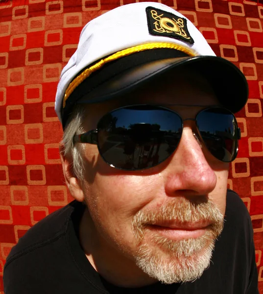 Man wearing a boat caption hat. Funny fish eye lens photo of a boat caption with a red checkered background.  happy captain on his boat.