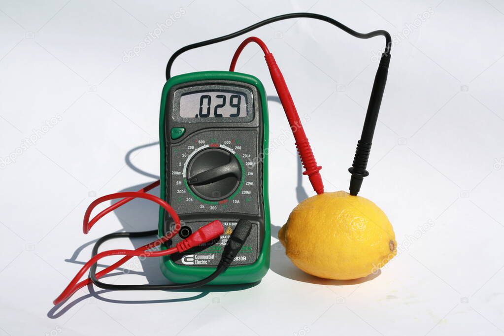 Volt Meter measuring Electrical Energy in a lemon. measurement of electric tension.  A lemon battery. A multi meter with positive and negative electrodes inserted into a lemon measures the bio electrical current created a fresh picked lemon.