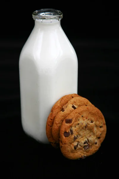 Milk and Cookies. Milk and Chocolate Chip Cookies. A retro bottle of fresh cold milk with one large chocolate chip cookie. milk bottle and cookies. good old fashioned foods and treats. Glass of milk and cookies isolated on black velvet.