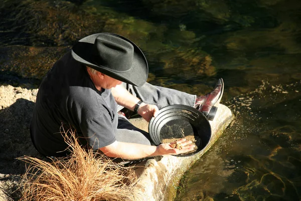 Gold Panning. gold panning man striking it rich by finding the mother lode or at least a nugget or two. A prospector looks into the pan looking for gold. golden nuggets. gold pan in the water with Gold. 24 karat gold. Gold Nuggets. Old Prospector.