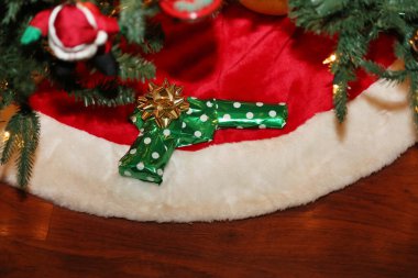 Christmas. Gun. Hand Gun Wrapped as a Christmas Present. Pistol Christmas Gift. Christmas Present of a Pistol Wrapped in green wrapping paper with a gold bow. 2020 saw a 45% increase in gun sales for the Christmas Holiday Season. Christmas Gun. 