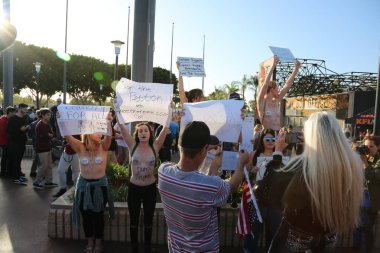 Costa Mesa, CA - 28 Nisan 2016: Meme ucunu serbest bırakın. Meme uçlarında bant olan kadınlar toplum içinde üstsüz olamamalarını protesto etmek için tişörtlerini çıkarıyorlar. Costa Mesa CA 'daki Donald J. Trump başkanlık mitinginde protesto eylemi. Donald Trump.