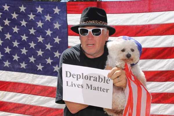 Deplorable Lives Matter. A man and his Bichon Frise Dog hold a Deplorable Lives Matter Sign. American Flag Background. Proud to be Deplorable. deplorable. Bichon Frise. Good Dog. Happy Dog. Lap Dog. Man\'s Best Friend. Puppy Dog. Deplorable Dog. Bark.