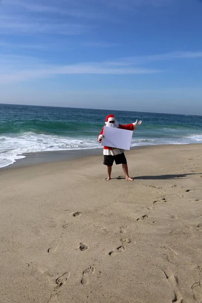 圣诞节 圣诞老人 带着白纸标志的圣诞老人在海滩 文字空间 圣诞老人拿着白纸标志 圣诞老人与空白标志隔离 给你的文字或形象留有空间 圣诞快乐 节日快乐 献上节日的问候 — 图库照片