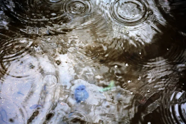 雨の嵐 雨が水たまりの中に滴り落ちる 雨が降り 雨が降る 青いレインコートと澄んだ傘を差した男が外に立っている 雨水を分散させるために雨具に取り付けられたホース — ストック写真