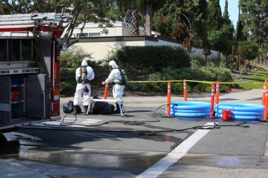 Lake Forest, California, Mayıs 2017: Tehlikeli madde ekibi, yüzme havuzu kimyasalları içeren tek bir kamyon kazasını temizliyor ve zehirli sıvıların çevreye salınmasını engelliyor. Tehlikeli madde kıyafetleri içinde itfaiye ve acil durum ekipleri.
