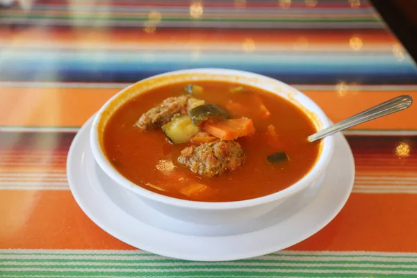 Mexican Food. Mexican Restaurant. ALBONDIGAS SOUP. Chips and Salsa. Mexican food Mexican soup with meat balls and vegetables. Mexican albondigas soup in a white ceramic bowl and plate on a traditional Mexican serape blanked table cloth and a spoon.