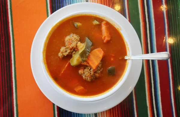 Mexican Food. Mexican Restaurant. ALBONDIGAS SOUP. Chips and Salsa. Mexican food Mexican soup with meat balls and vegetables. Mexican albondigas soup in a white ceramic bowl and plate on a traditional Mexican serape blanked table cloth and a spoon.