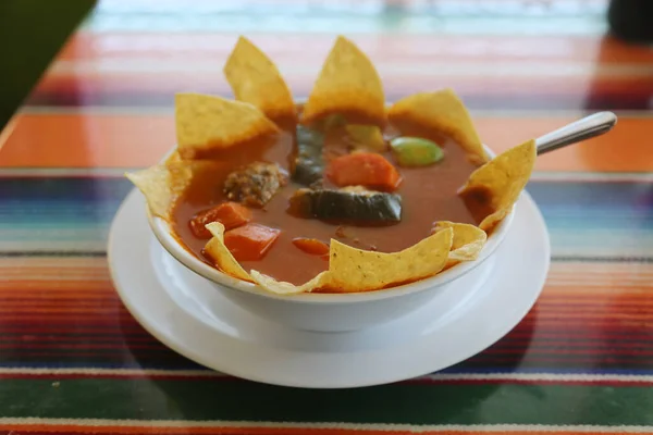 Mexican Food. Mexican Restaurant. ALBONDIGAS SOUP. Chips and Salsa. Mexican food Mexican soup with meat balls and vegetables. Mexican albondigas soup in a white ceramic bowl and plate on a traditional Mexican serape blanked table cloth and a spoon.