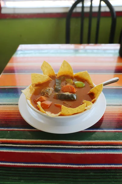 Mexican Food. Mexican Restaurant. ALBONDIGAS SOUP. Chips and Salsa. Mexican food Mexican soup with meat balls and vegetables. Mexican albondigas soup in a white ceramic bowl and plate on a traditional Mexican serape blanked table cloth and a spoon.