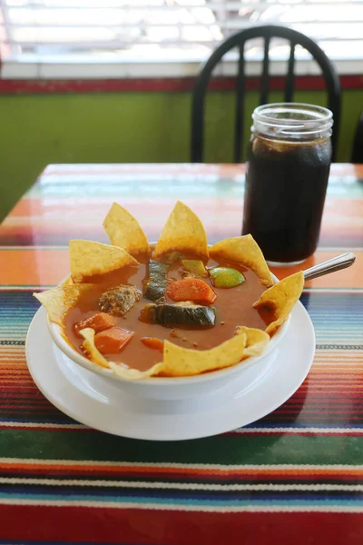 Mexican Food. Mexican Soup. Traditional Mexican food Mexican soup with meat balls and vegetables. Mexican albondigas soup in a white ceramic bowl and plate on a traditional Mexican serape blanked table cloth and a spoon. Chips. Chips and Salsa. Food.
