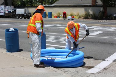 Tehlikeli madde. Lake Forest, California, 23 Mayıs 2017: Tehlikeli madde ekibi, yüzme havuzu kimyasalları içeren tek bir kamyon kazasını temizler ve zehirli sıvıların çevreye salınmasını önler. Tehlikeli madde kıyafetleri içinde itfaiye ve acil durum ekipleri. 