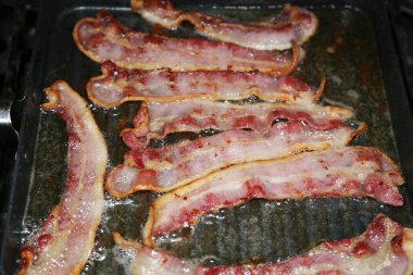 Bacon being grilled in a pan on a barbeque grill