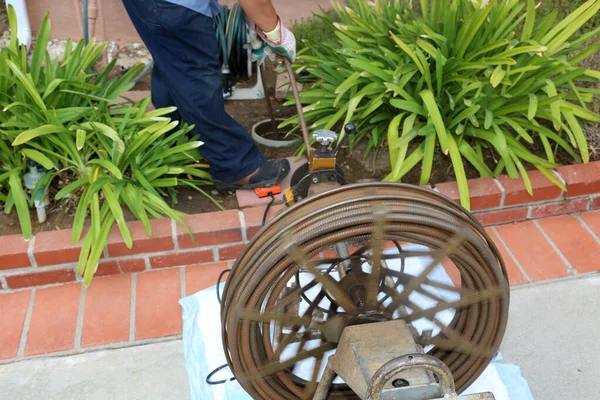 Sewer cleaning. A plumber uses a sewer snake to clean blockage in a sewer line. Plumber holding a drain pipe, providing sewer cleaning service outdoor. Sewage pumping machine is unclogging blocked drain. Plumbing Service. Drain Cleaning. Sewer Drain.