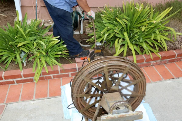 Sewer cleaning. A plumber uses a sewer snake to clean blockage in a sewer line. Plumber holding a drain pipe, providing sewer cleaning service outdoor. Sewage pumping machine is unclogging blocked drain.