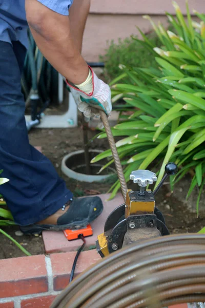 Sewer cleaning. A plumber uses a sewer snake to clean blockage in a sewer line. Plumber holding a drain pipe, providing sewer cleaning service outdoor. Sewage pumping machine is unclogging blocked drain.