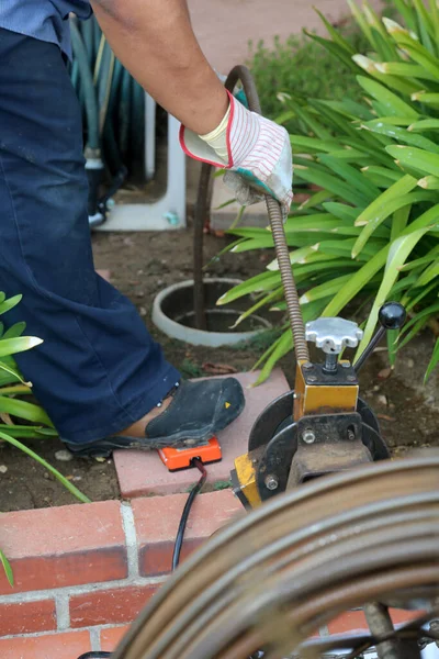 Sewer cleaning. A plumber uses a sewer snake to clean blockage in a sewer line. Plumber holding a drain pipe, providing sewer cleaning service outdoor. Sewage pumping machine is unclogging blocked drain. Plumbing Service. Drain Cleaning. Sewer Drain.