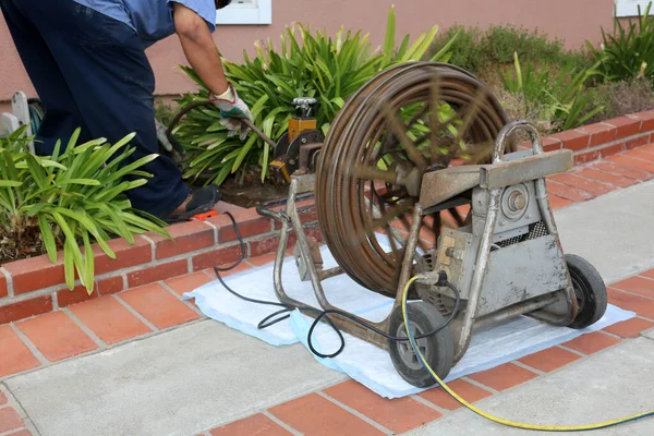 Sewer cleaning. A plumber uses a sewer snake to clean blockage in a sewer line. Plumber holding a drain pipe, providing sewer cleaning service outdoor. Sewage pumping machine is unclogging blocked drain. Plumbing Service. Drain Cleaning. Sewer Drain.