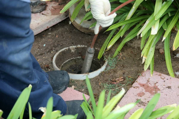 Sewer cleaning. A plumber uses a sewer snake to clean blockage in a sewer line. Plumber holding a drain pipe, providing sewer cleaning service outdoor. Sewage pumping machine is unclogging blocked drain. Plumbing Service. Drain Cleaning. Sewer Drain.