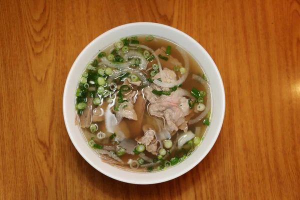 Vietnamese rice noodle soup with sliced rare beef.  Vietnamese Cuisine - Beef Pho Noodle Soup or Pho Bo Soup. Served with Fresh Greens in White Bowl on Wooden Table. Pho Bo Soup with Spicy Sauces. Soup for Lunch. Soup for Dinner. Soup for a Snack.