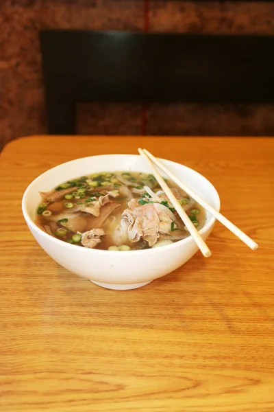 Vietnamese rice noodle soup with sliced rare beef.  Vietnamese Cuisine - Beef Pho Noodle Soup or Pho Bo Soup. Served with Fresh Greens in White Bowl on Wooden Table. Pho Bo Soup with Spicy Sauces. Soup for Lunch. Soup for Dinner. Soup for a Snack.