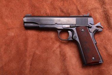 45 caliber 1911 semi automatic pistol. 1911 .45 caliber army pistol on brown leather background.