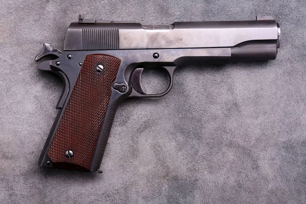 45 caliber 1911 semi automatic pistol. Vintage 1911 .45 caliber pistol on blue grey leather background.