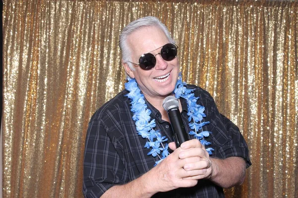 A man sings a song. A man sings into a microphone while posing for his portrait in a Photo Both with a Gold Sequin Background Curtain.