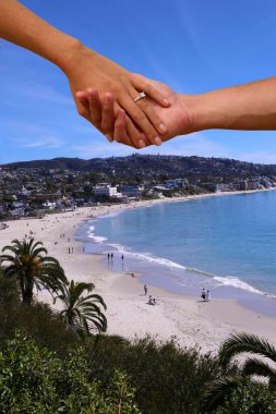 Engagement Couple holding hands with a beach background. A couple hold hands with a wedding ring and Laguna Beach California Background.