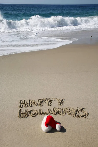 Santa Hat. Santa Claus hat on the beach with the words HAPPY HOLIDAYS written in the sand. Room for text. Words can be removed and replaced with your own.