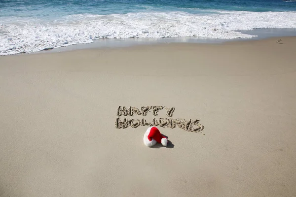 Santa Hat. Santa Claus hat on the beach with the words HAPPY HOLIDAYS written in the sand. Room for text. Words can be removed and replaced with your own.