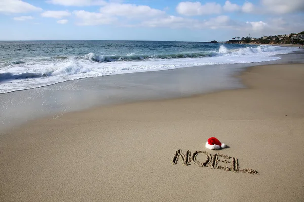 Santa Hat. Santa Claus hat on the beach with the word NOEL written in the sand. Room for text. Words can be removed and replaced with your own.