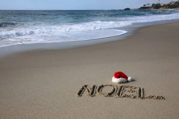 Santa Hat. Santa Claus hat on the beach with the word NOEL written in the sand. Room for text. Words can be removed and replaced with your own.