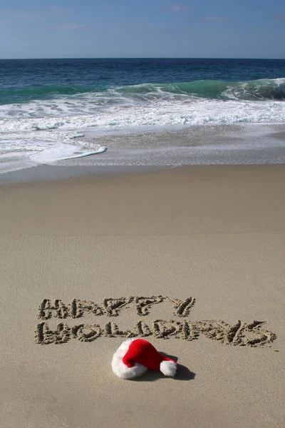 Santa Hat. Santa Claus hat on the beach with the words HAPPY HOLIDAYS written in the sand. Room for text. Words can be removed and replaced with your own.